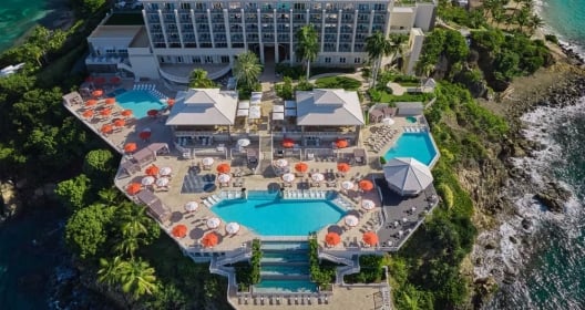 Aerial view of pool with umbrellas and hotel.