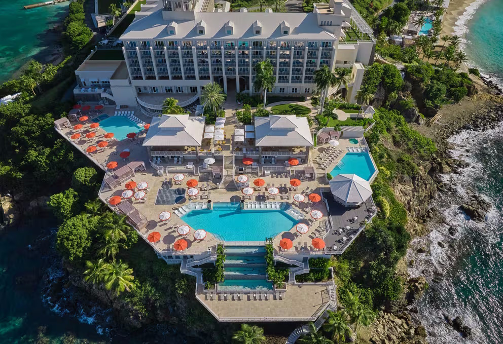 Aerial view of pool with umbrellas and hotel.